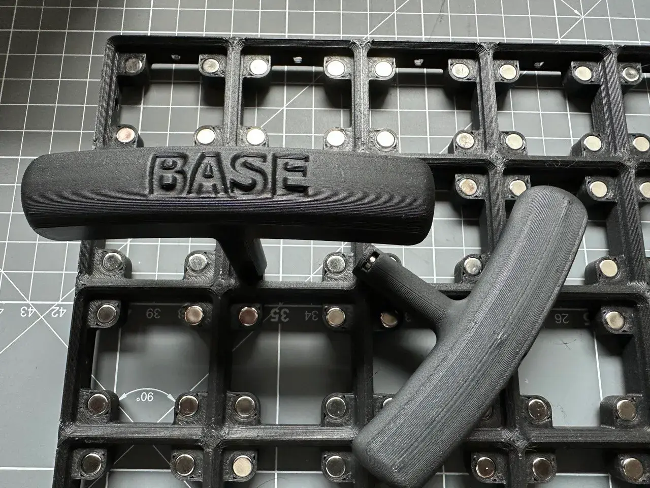 A simple magnet jig with a palm handle inscribed with the word 'BASE'.